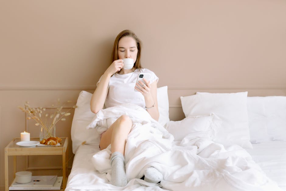woman reading her phone in bed drinking coffee